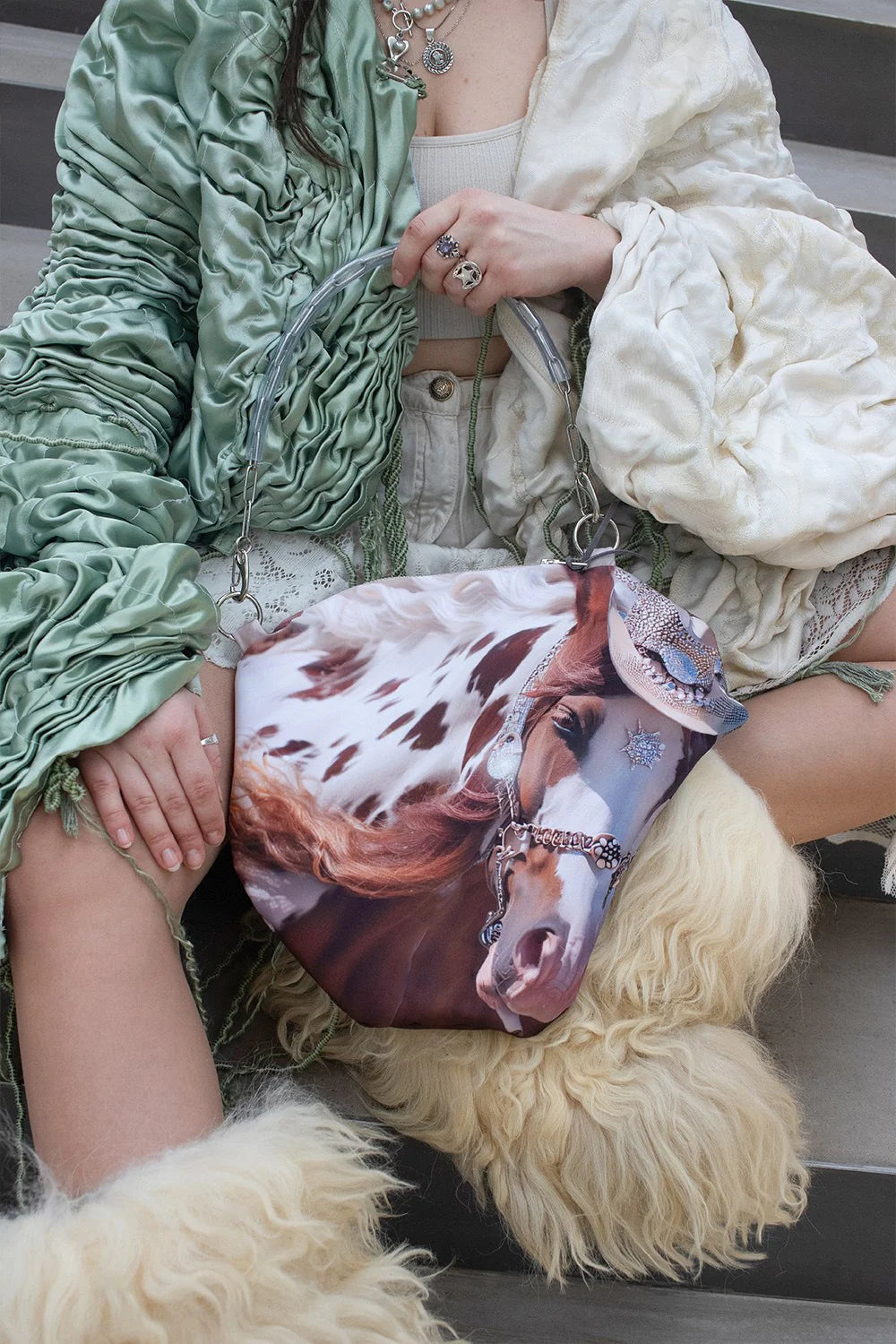Person holding a bag with a horse print, wearing a green coat and white fur garment.