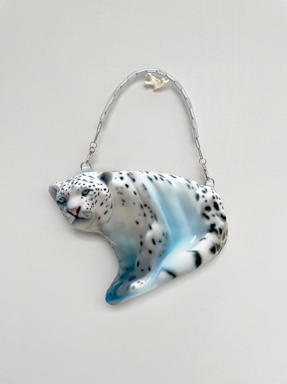 Glass ornament of a snow leopard with a blue and white design on a light gray background