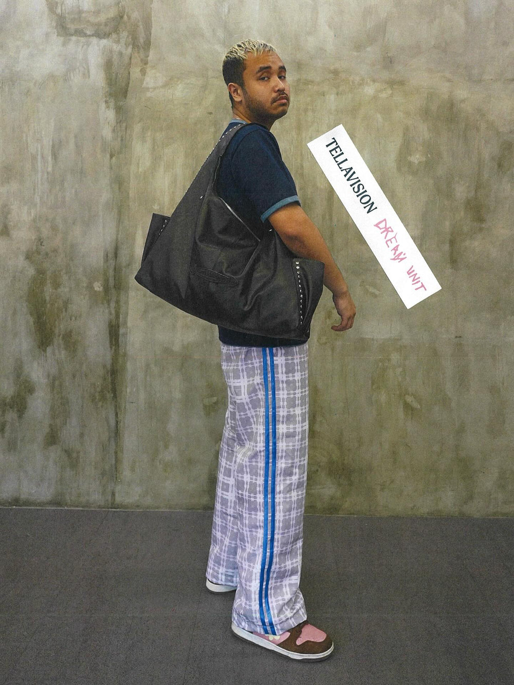 Person holding a black bag against a textured wall with a label.