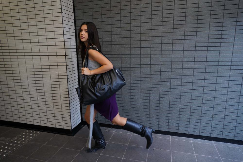 Woman holding a black handbag against a tiled wall.