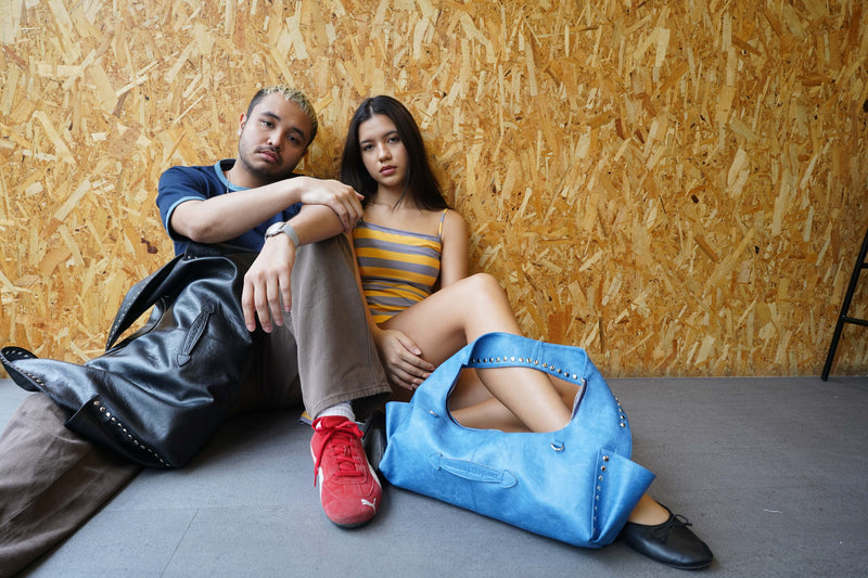Two people sitting on the floor against a wooden wall with a blue bag.