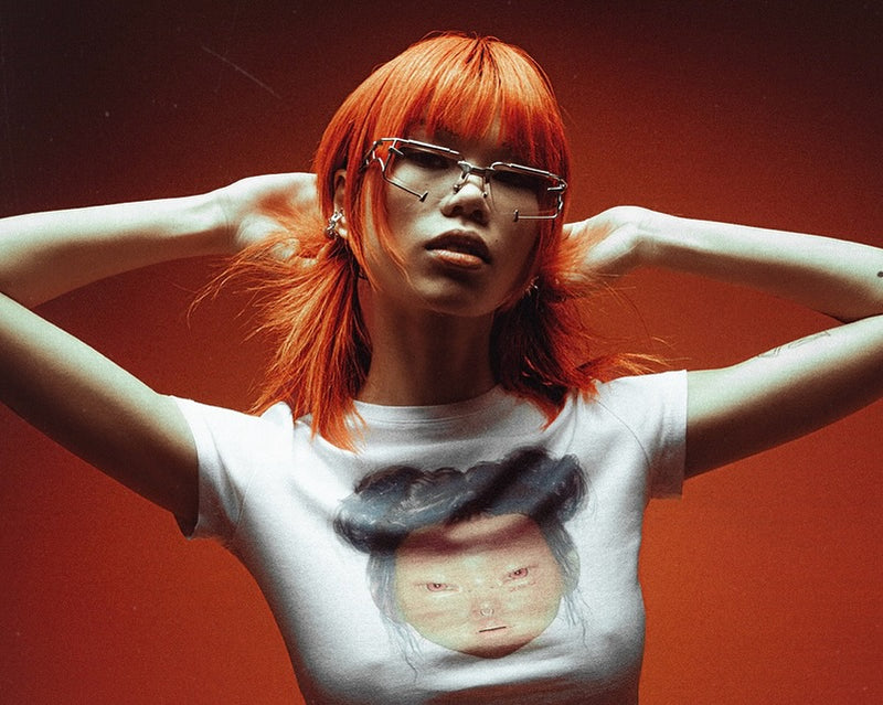 Person with red hair wearing a white t-shirt with a graphic design against a red background