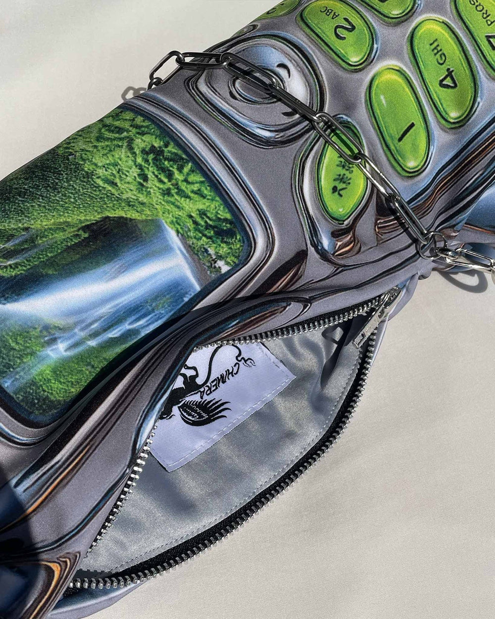 Close-up of a metallic pouch with green accents and a scenic reflection, featuring a brand logo.