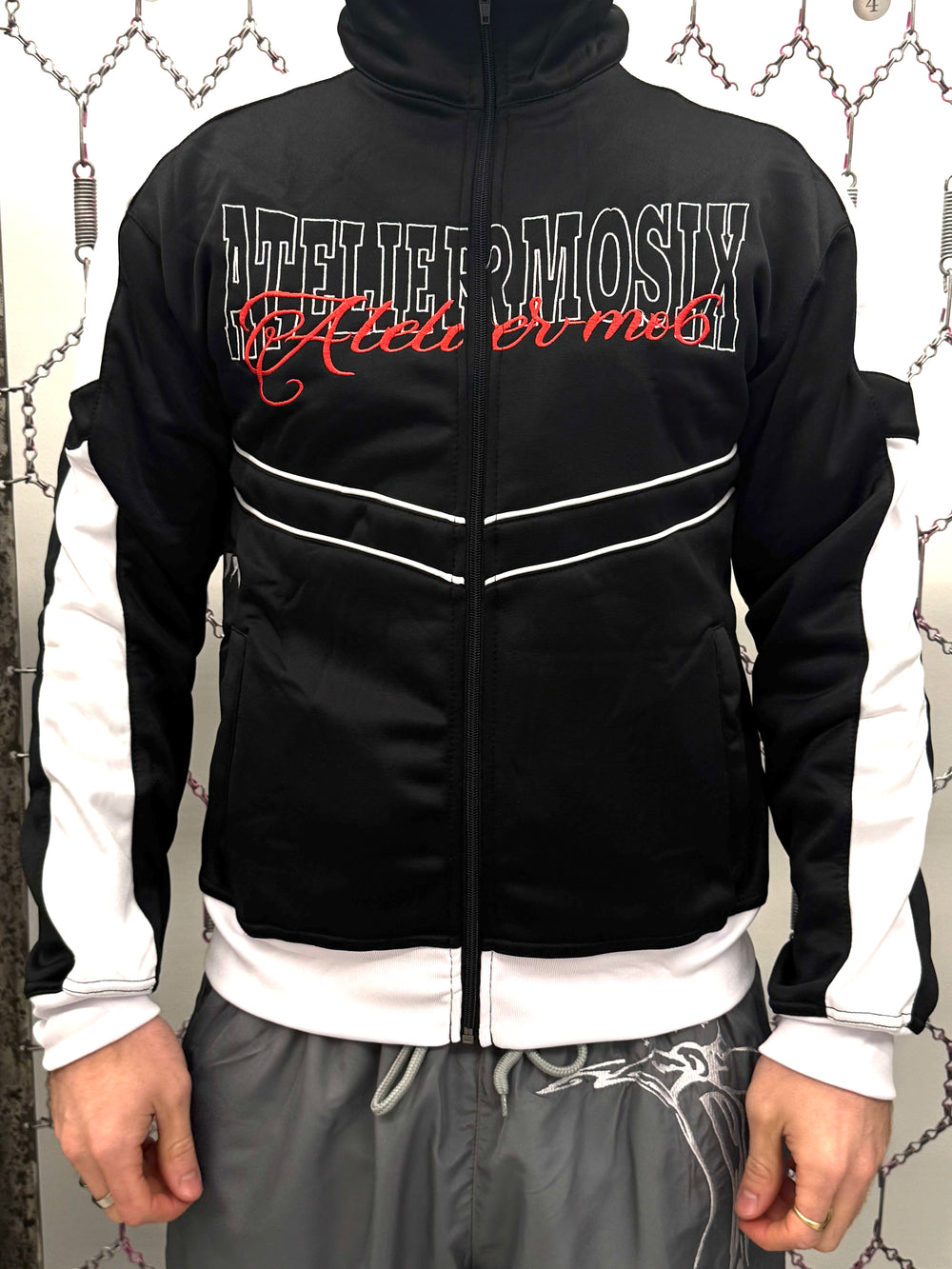 Zwarte streetwear track jacket met high-neck ritssluiting, contrast zijpanelen en grafische frontprint, premium midweight stof met geborduurde sterdetails en ribboorden, urban fashion Nederland.