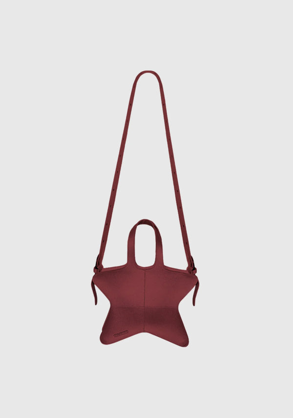 Wine red star-shaped shoulder bag with adjustable long strap and structured leather finish displayed on light grey background.