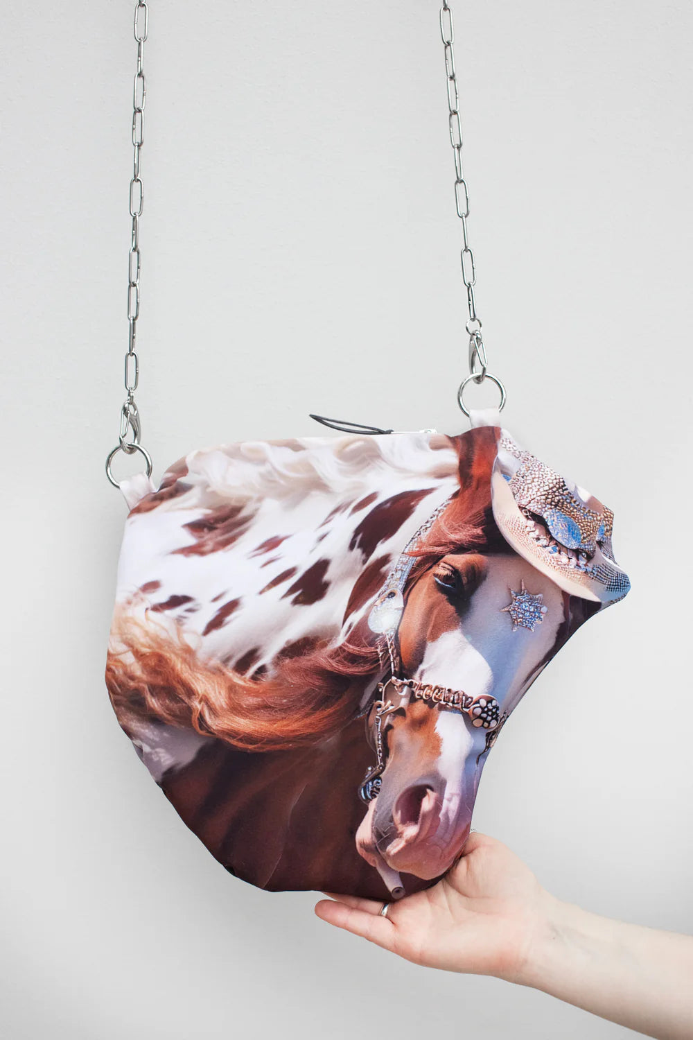 Handbag with a horse design held by a hand against a light gray background