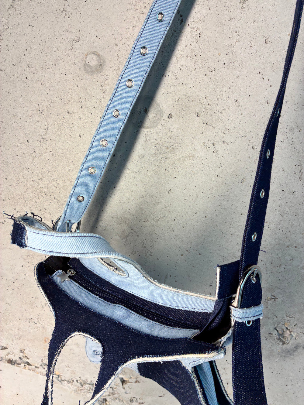 Close-up detail of patchwork denim star bag showing adjustable strap, zipper closure, and raw edge stitching.