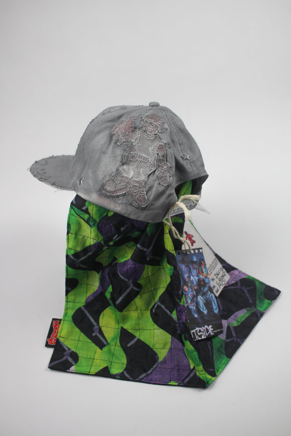 Grey distressed baseball cap with embroidered graphic and attached quilted scarf panel in green and purple print.