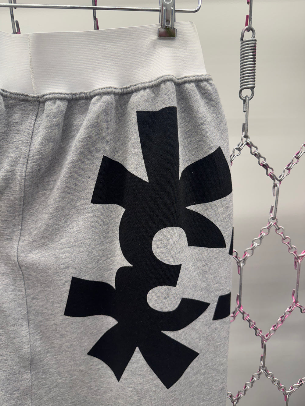 Gray sweatpants with a black symbol on a hanger against a metallic chain background