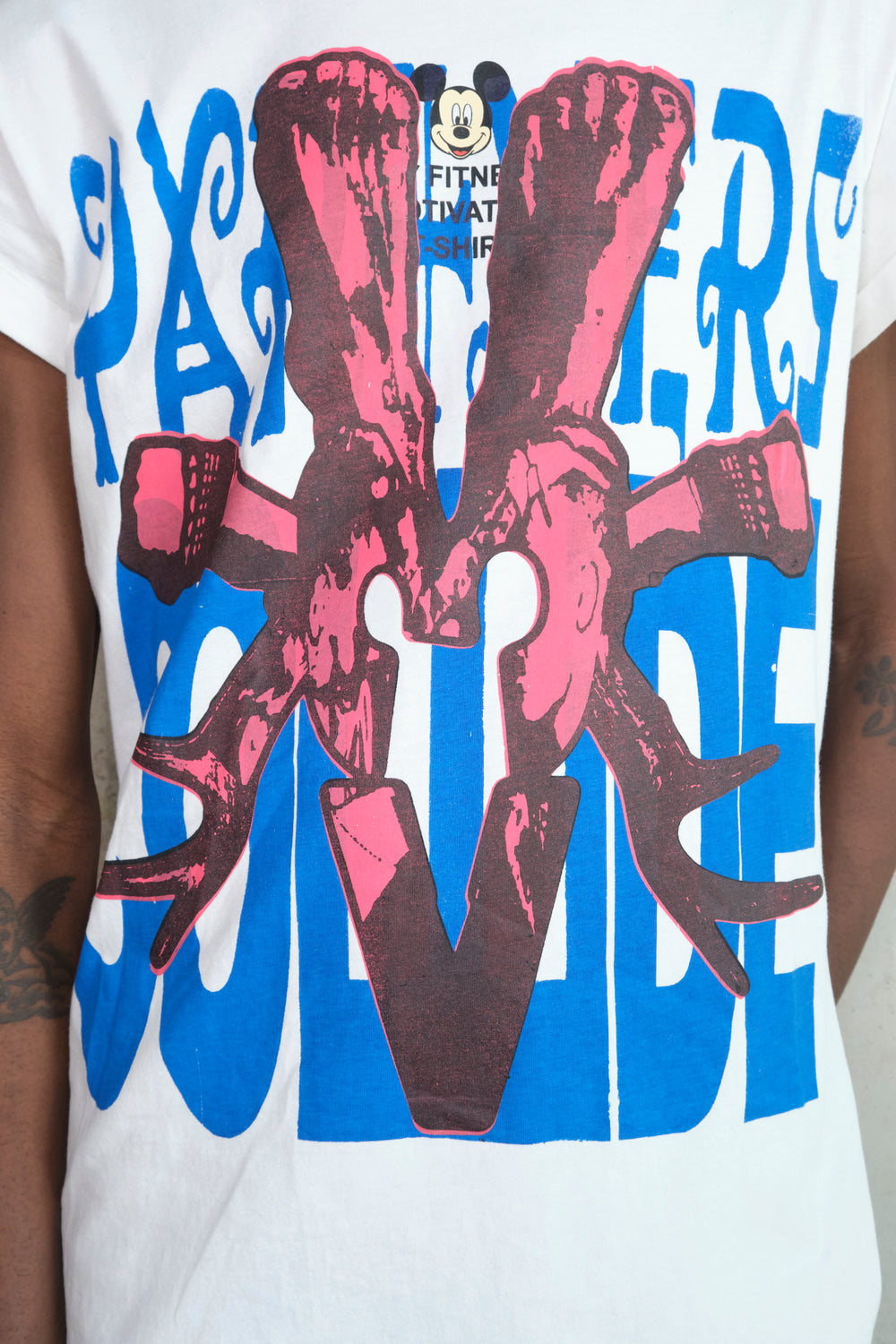 Close-up of a person wearing a white Gatto T-shirt with a bold screenprint design. The print features large red skeletal hands gripping wrenches, intertwined over blue block letters spelling PARTNERS COLLIDE. The shirt has rolled-up sleeves and a relaxed fit, adding to its casual, edgy aesthetic.