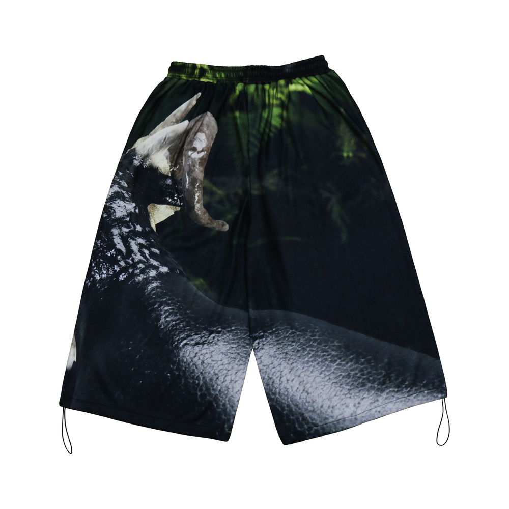 Long shorts featuring a bold nature-inspired print, depicting lush green foliage and a photorealistic image of an animal’s open mouth. The design has a dark, earthy tone with drawstrings on the waistband and hems, creating an adjustable, relaxed fit that merges outdoor aesthetics with urban style.