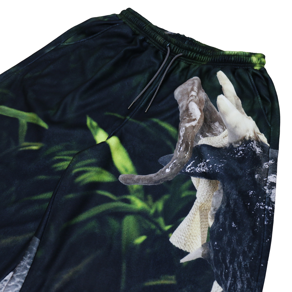 Close-up of shorts featuring a vivid, nature-inspired print with lush green foliage and a detailed image of an animal's open mouth. The shorts have an elastic waistband with drawstrings for an adjustable fit, blending an outdoor aesthetic with functional design elements for a bold and unique look