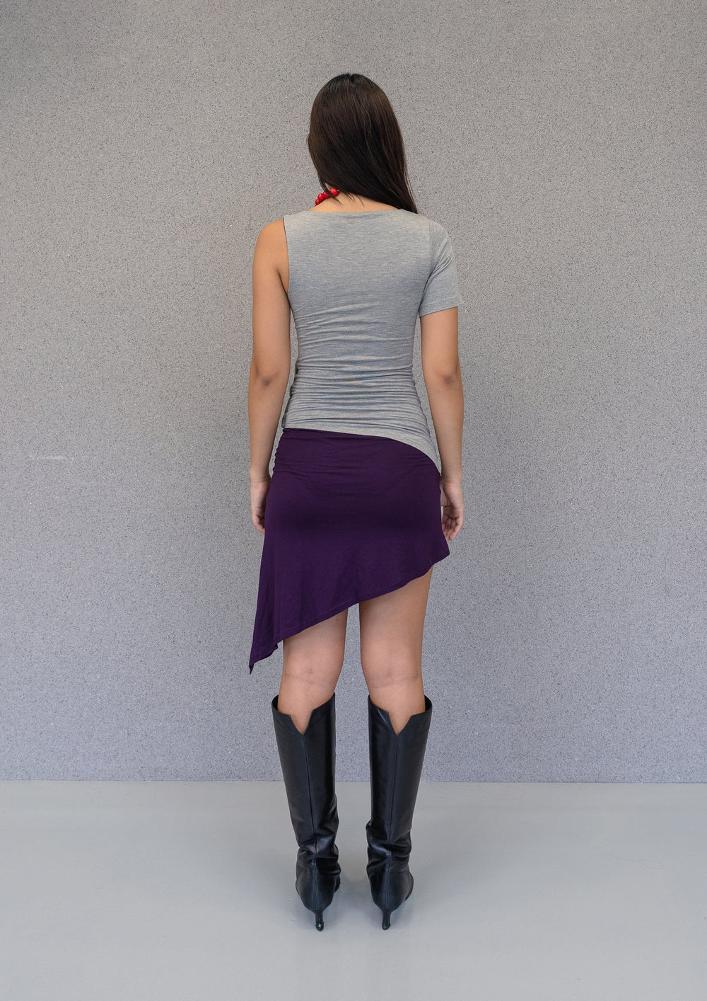 Back view of fitted grey and purple asymmetrical mini dress with uneven hemline and single short sleeve.
