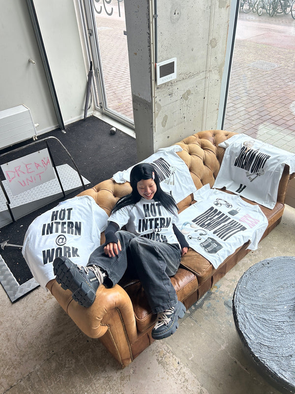 Person sitting on a brown couch wearing a 'Not Intern Work' shirt with printed text and graphics.
