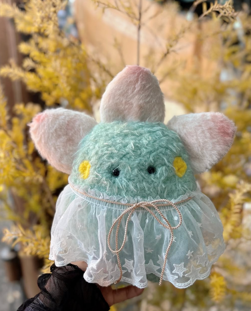 Mint green plush creature with starry tulle dress and pastel ears, standing on a wooden platform among tree roots – handmade Mimi Planet collectible toy in forest setting