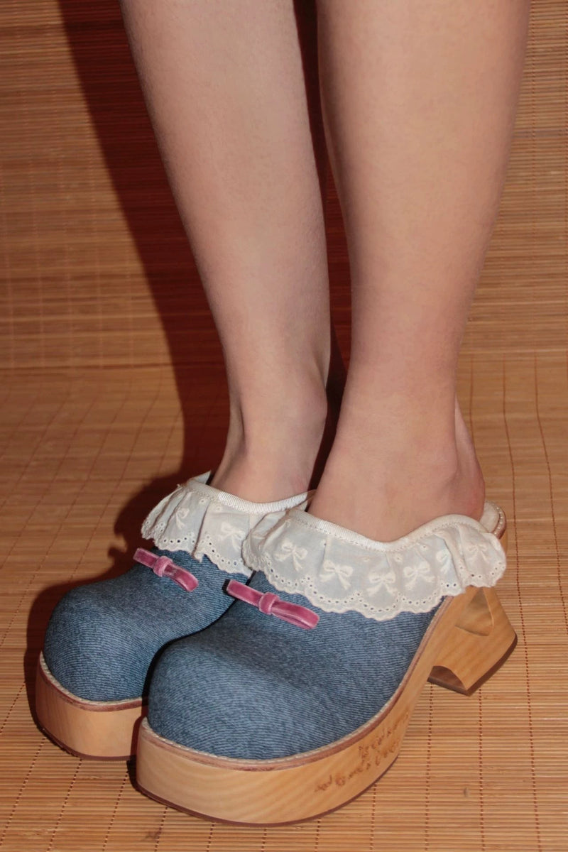 Blue denim shoes with wooden soles and lace trim on a wooden floor.