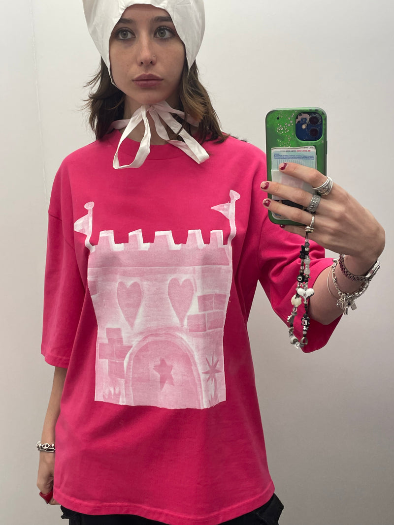 Person wearing a bright pink shirt with a white graphic design, holding a phone.