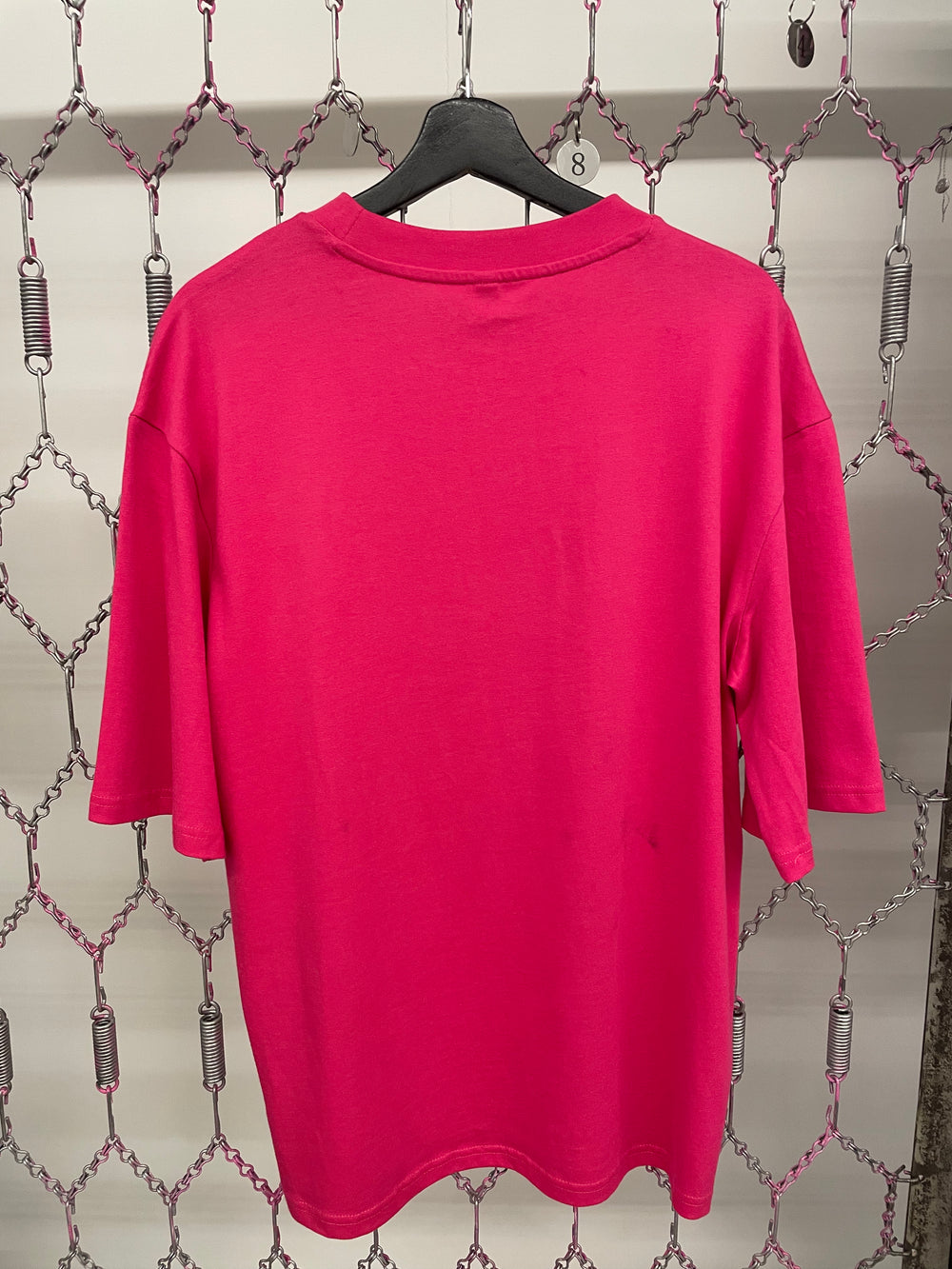 Pink shirt on a hanger against a chain-link fence background