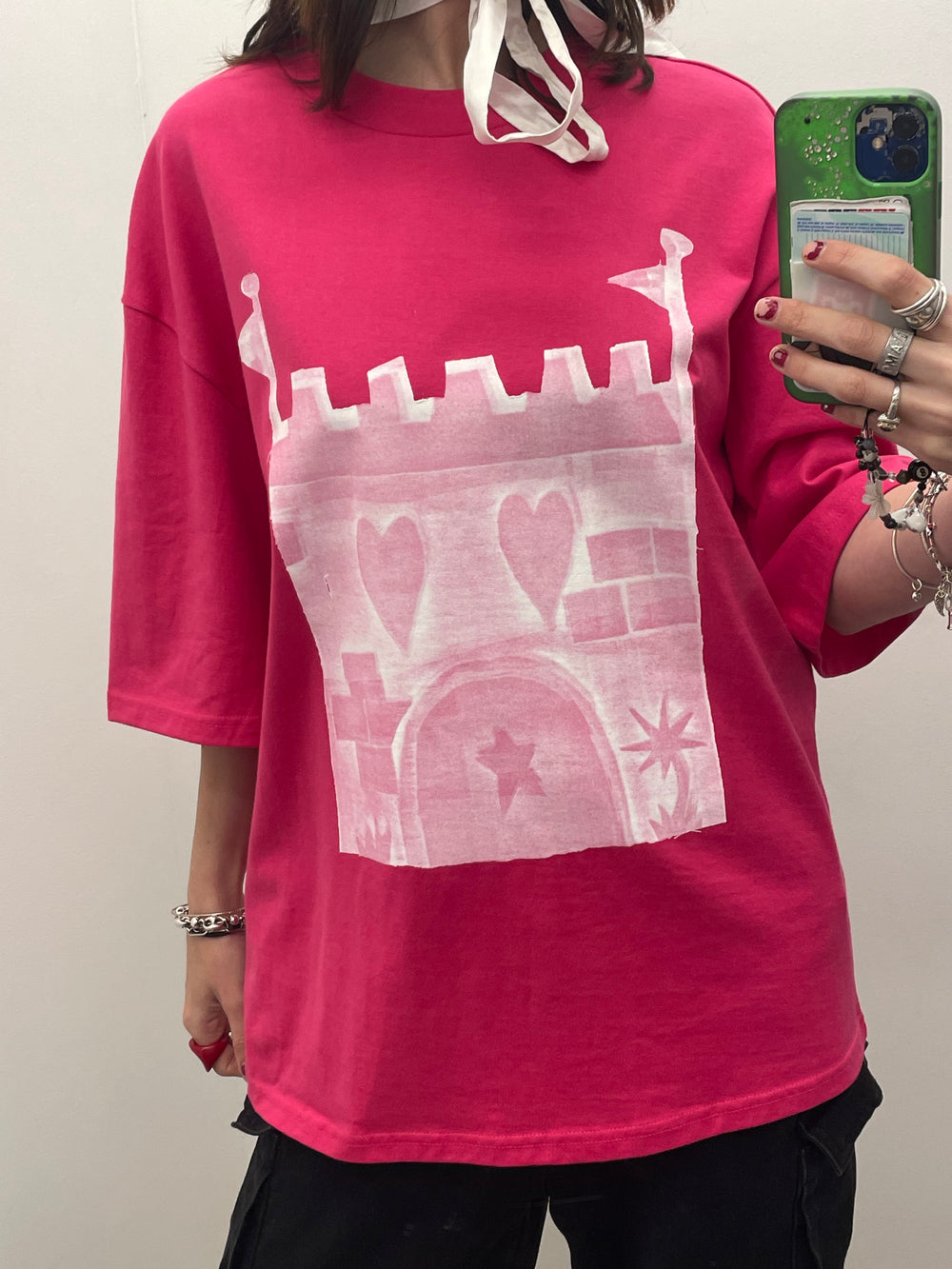 Person wearing a pink sweatshirt with a white castle design, holding a phone.
