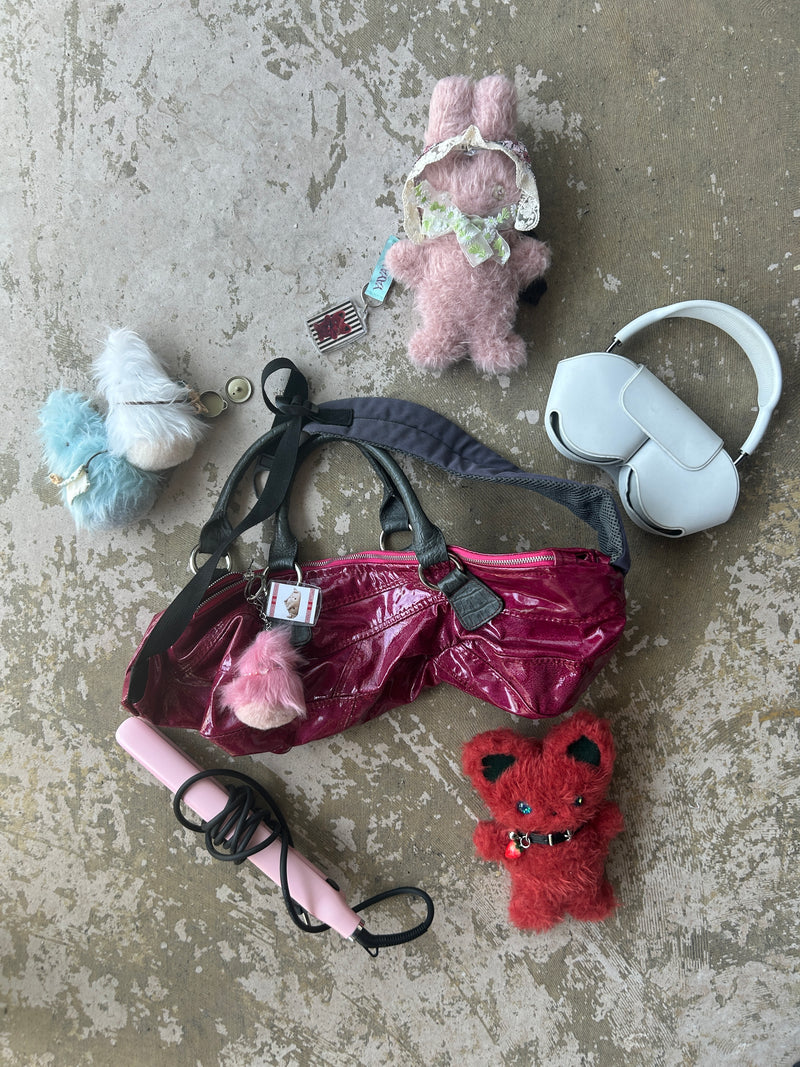Flat lay of kawaii Mimi Planet plush toys with accessories – pink and red bunnies, blue fluffy creature, burgundy handbag, white headphones, pink hair straightener, and decorative keychains on concrete floor.