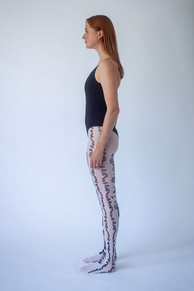 Model wearing white graphic patterned tights with brown swirl print, side view.