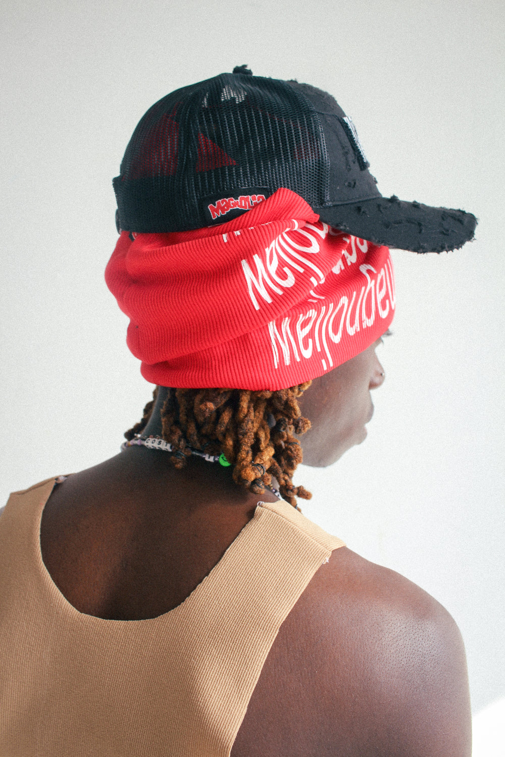 Black mesh baseball cap worn with red knit scarf layered underneath, side back view.