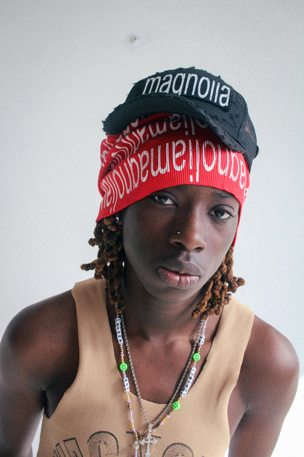 Black mesh baseball cap with white embroidered text worn over red knit scarf, front view.