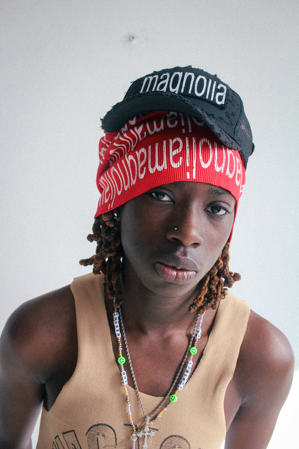 Black mesh baseball cap with white embroidered text worn over red knit scarf, front view.