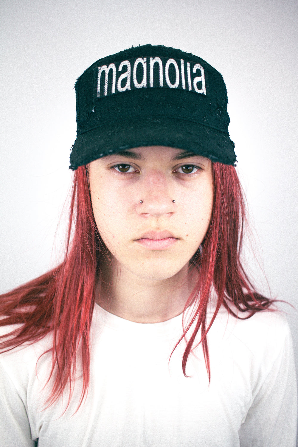 Black distressed baseball cap with white “magnolia” embroidery, worn front view.