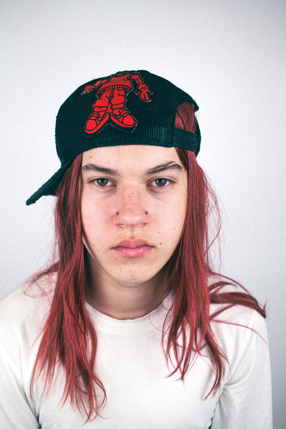 Black mesh baseball cap with red embroidered character graphic worn sideways, side view.