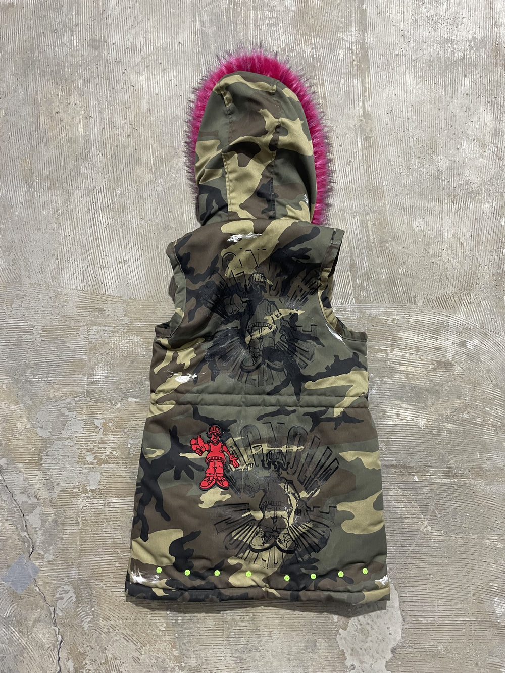 Camouflage hooded padded vest, back view, featuring printed graphics and bright pink faux fur hood trim.