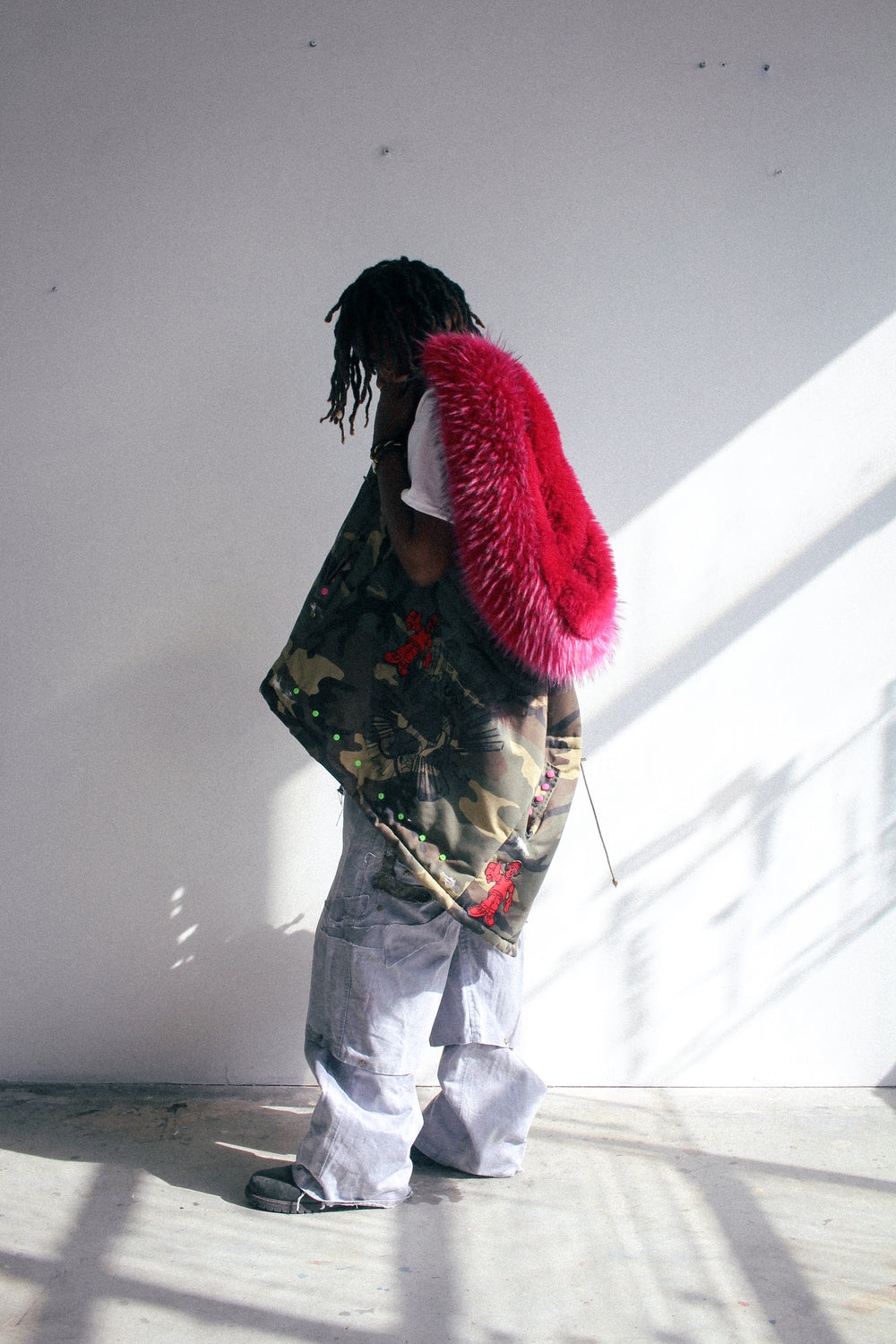 Camouflage hooded padded vest worn, side view showing oversized pink faux fur hood trim and graphic details.