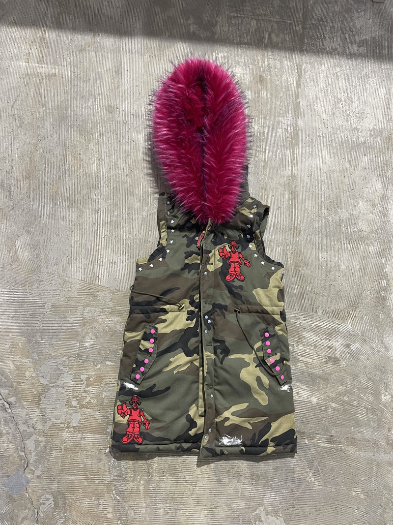 Camouflage hooded padded vest, front view, with snap-button closure, graphic patches, stud details, and pink faux fur hood trim.