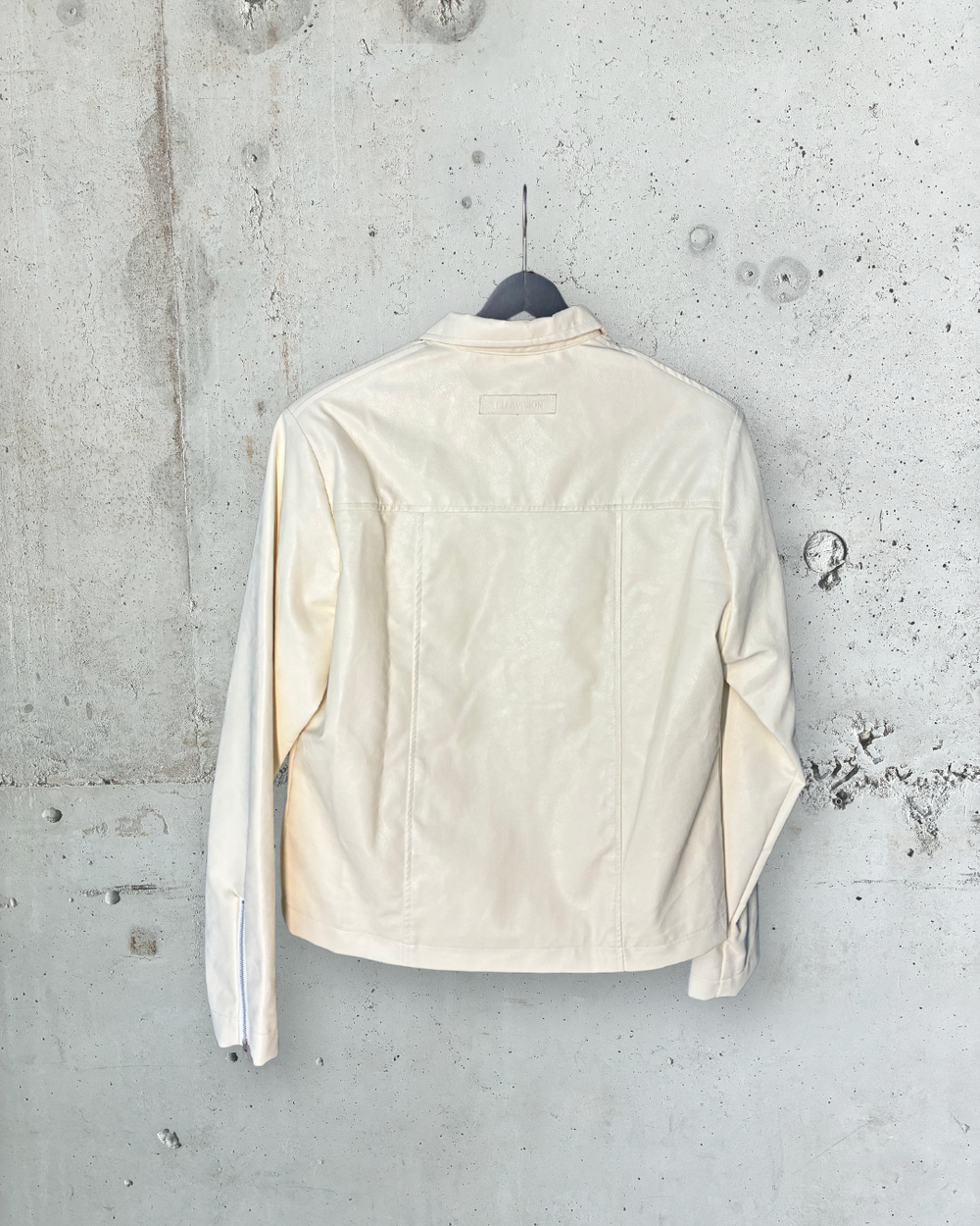Back view of cream faux leather jacket by Tellavision with clean panel detailing and minimal silhouette.