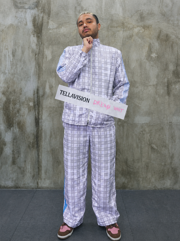 Model wearing pastel tartan Tellavision zip-up jacket with matching relaxed trousers holding Dream Unit sign.