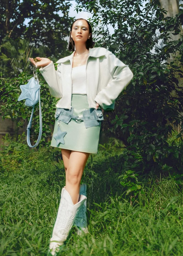 Woman in light green jacket and skirt holding a denim bag in a forest setting