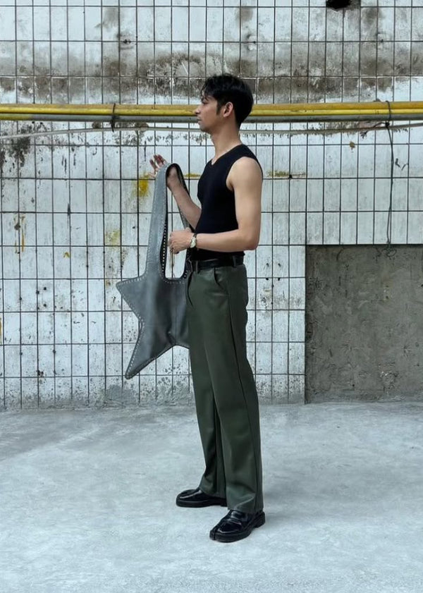 Person holding a large gray bag against a concrete wall.
