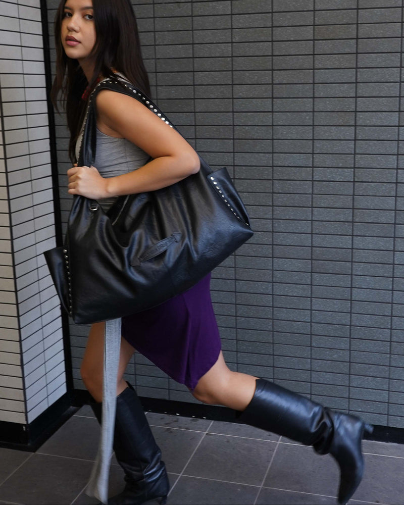 Woman holding a black handbag against a tiled wall.