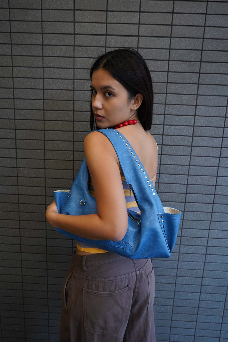 Woman wearing a blue sleeveless top with a yellow shirt underneath, standing against a tiled wall.