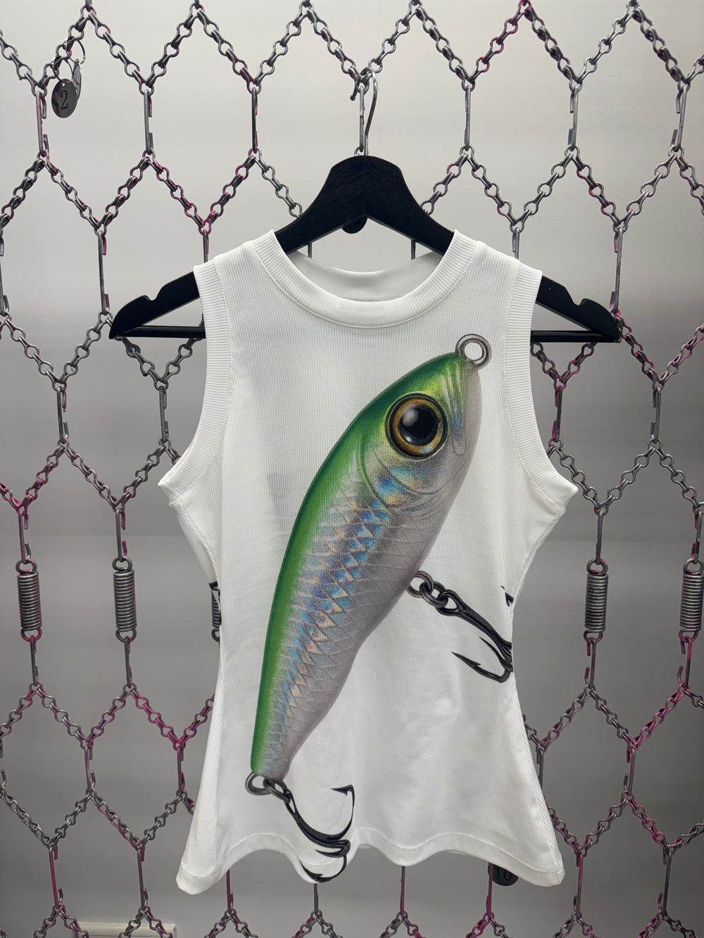 White sleeveless shirt with a fishing lure design on a chain-link fence background