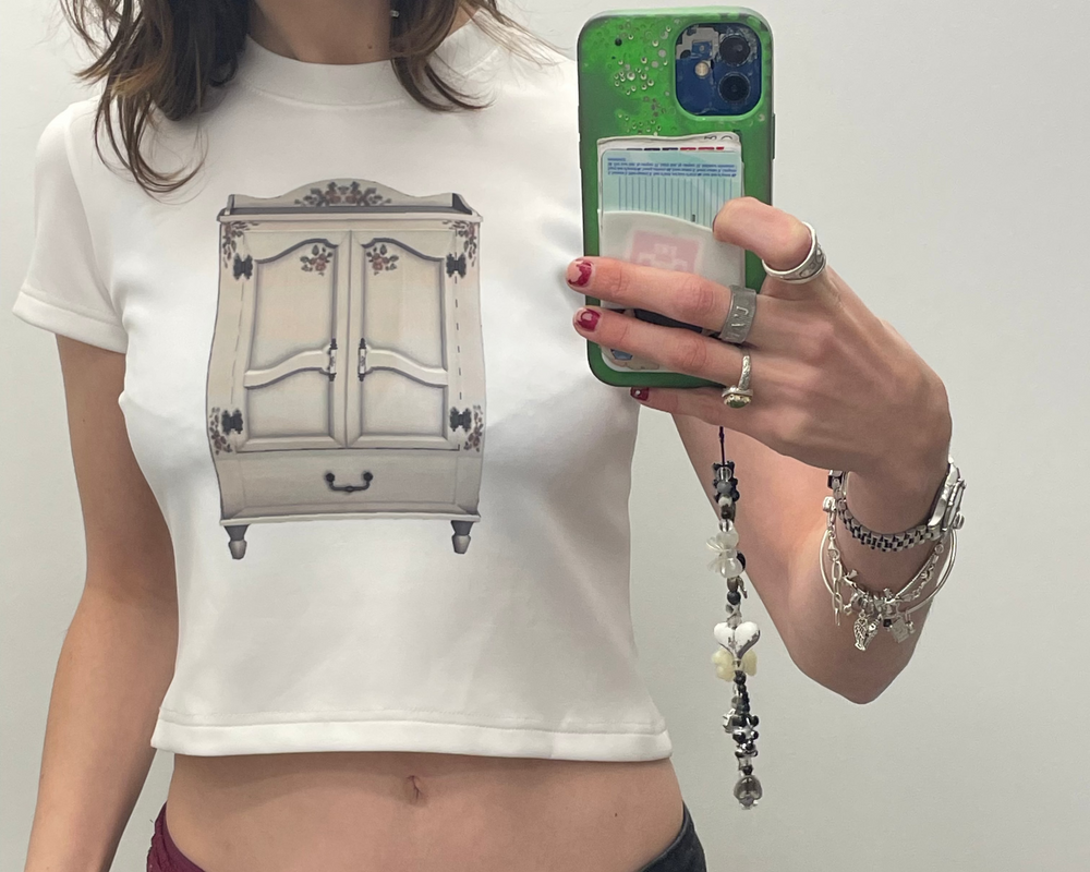 Person wearing a white t-shirt with a dresser graphic, holding a phone.