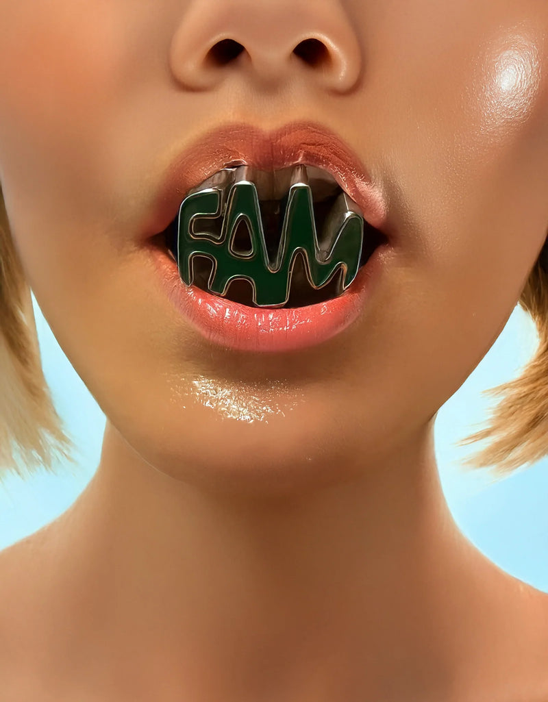 Close-up of a person wearing a green and black 'FAM' lip ring against a blue background