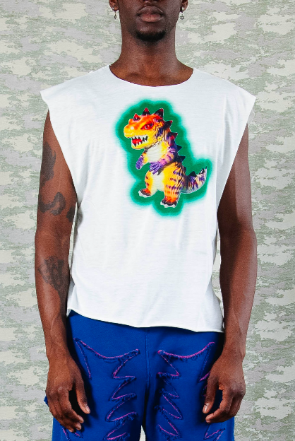 Model wearing white sleeveless t-shirt with colorful neon dinosaur graphic, paired with electric blue pants featuring zigzag stitch details – posed against camo-patterned background