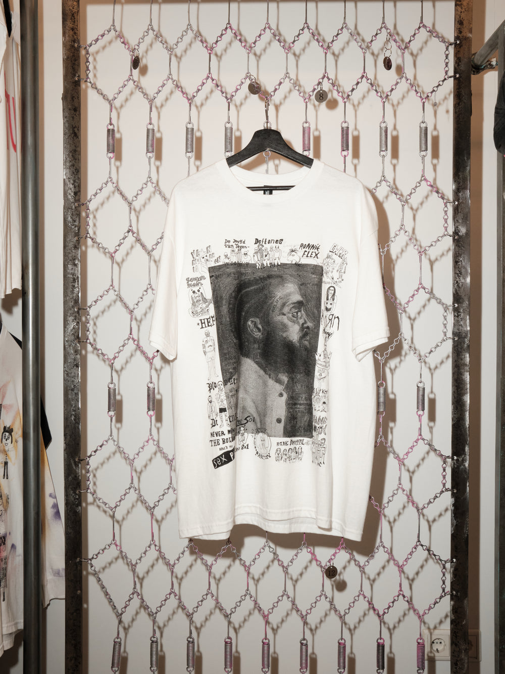 White t-shirt with graphic design on a hanger against a patterned wall.