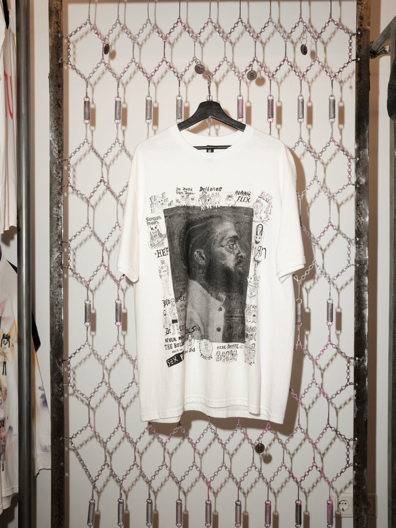 White t-shirt with graphic design on a hanger against a patterned wall.