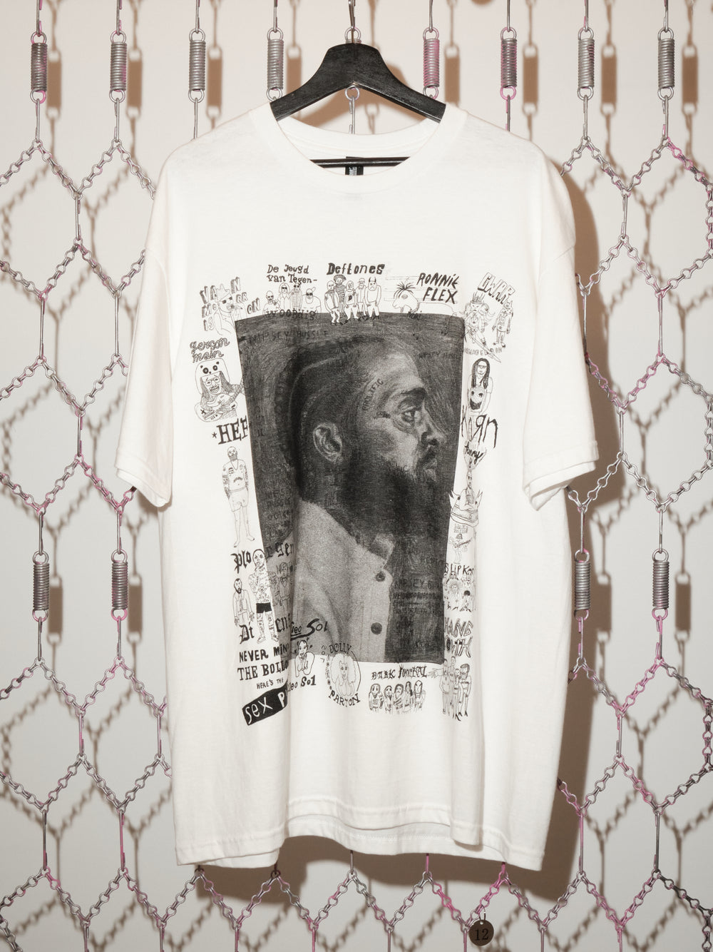 White t-shirt with graphic design on a hanger against a patterned wall.