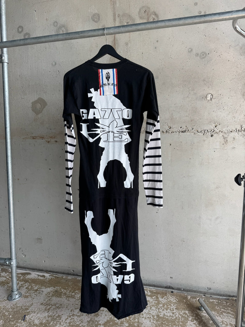 Back view of black long dress featuring bold white GATTO graphic print with abstract figures, striped long sleeves, and red-white-blue stitched label at the neckline, with a distressed hem for an edgy streetwear look