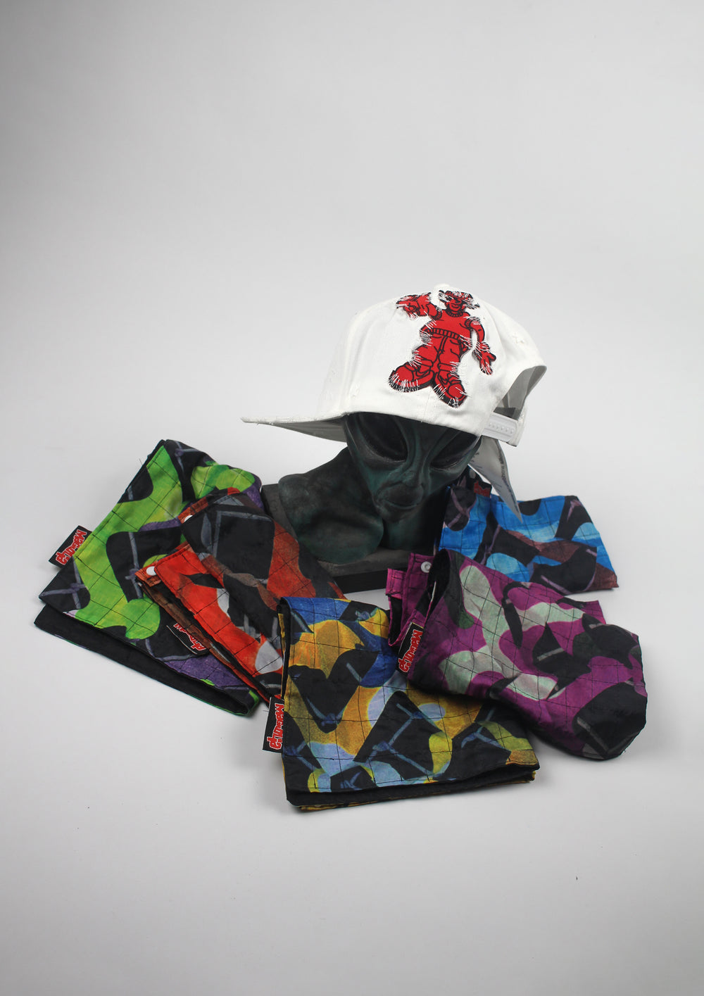 White distressed baseball cap with red graphic embroidery, displayed with multiple quilted Banada panels in assorted color prints.