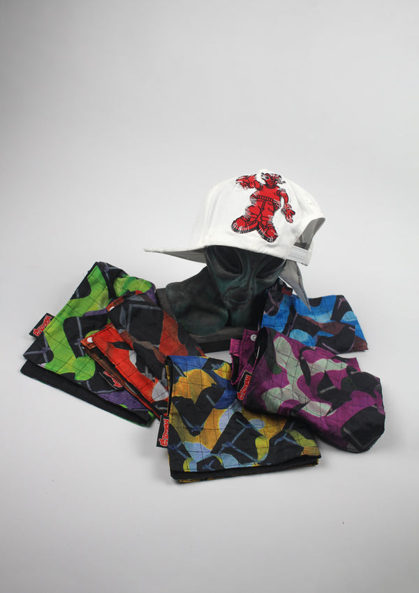 White distressed baseball cap with red graphic embroidery, displayed with multiple quilted Banada panels in assorted color prints.