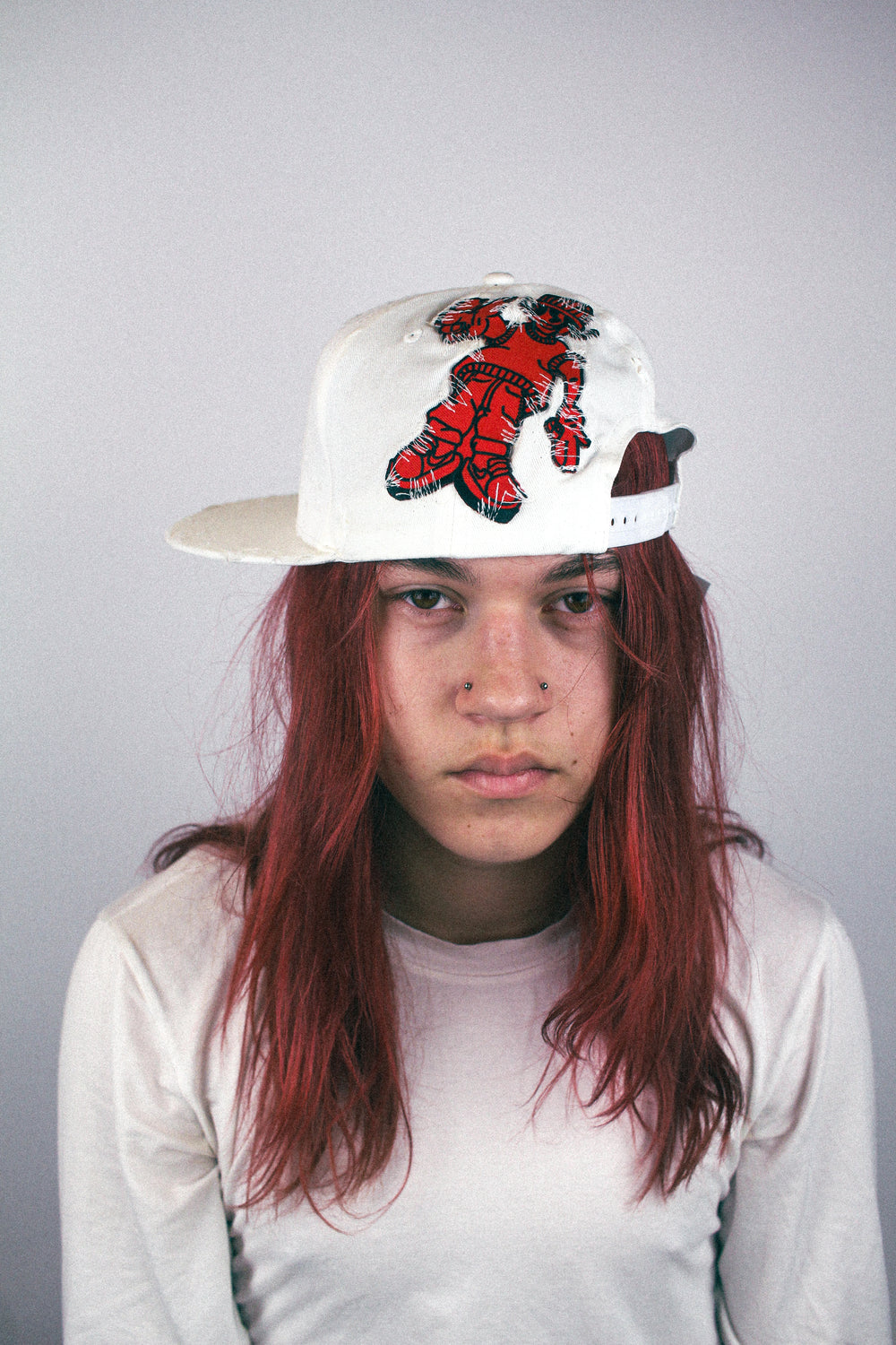 White distressed baseball cap with red embroidered character graphic, worn front view.